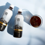 Overhead view of two bottles labeled Black Coffee Dark Roast and a glass of iced coffee on a pale blue surface