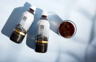 Overhead view of two bottles labeled Black Coffee Dark Roast and a glass of iced coffee on a pale blue surface