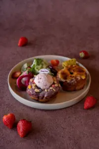 d70f59a79d5dd85fea4f958fcefa48a2 | コーヒーステーション Dessert plate with a chocolate glazed donut topped with ice cream and crunchy bits plus a pastry greens salad and strawberries on a beige plate and mauve background