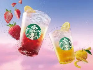 Two iced Starbucks drinks with strawberries and lemon slices splashing in a colorful sky