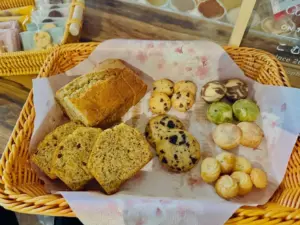 da0e472ab3920662f0206dd2cb606e30 | コーヒーステーション Basket of assorted baked goods sliced banana loaf chocolate chip cookies and small round cookies on parchment paper in a wicker basket