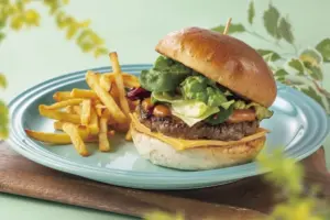 Juicy cheeseburger with lettuce and tomato on a glossy brioche bun with fries on a turquoise plate