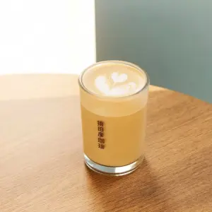 Latte in a clear glass on a wooden table topped with heart shaped latte art The glass has vertical text in dark characters on its side