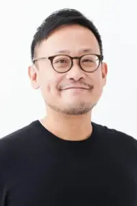 Smiling man with round glasses and short dark hair wearing a black shirt against a white background