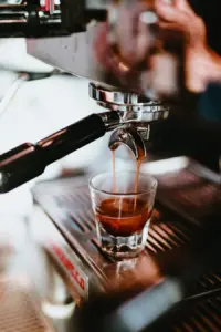 Close up of an espresso machine pouring two streams of dark coffee into a glass taza under a portafilter