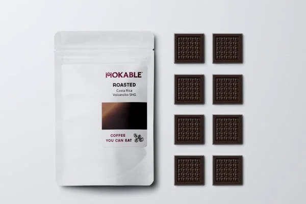 MOKABLEの「食べられるコーヒー」と書かれた白いパッケージと、小さな四角いチョコレートが8個、白い背景に整然と並べられています。