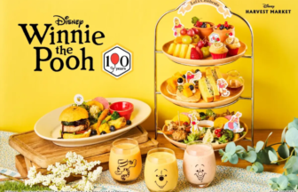 Winnie the Pooh 100th anniversary food display tiered tray of desserts a plate with a burger three face decorated drinks on a yellow background