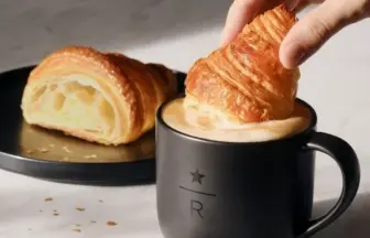 Croissant being dipped into a black mug of coffee while another croissant rests on a plate beside it