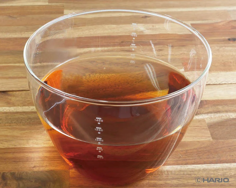 2275123b7d7e2f14fa9b37d43bdd21d6ac69a83800x640 | コーヒーステーション Clear glass measuring cup filled with amber liquid sits on a wooden countertop showing measurement marks along the side