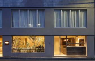 Modern twostory building facade ground floor glass windows reveal a warmly lit interior with plants and a reception area