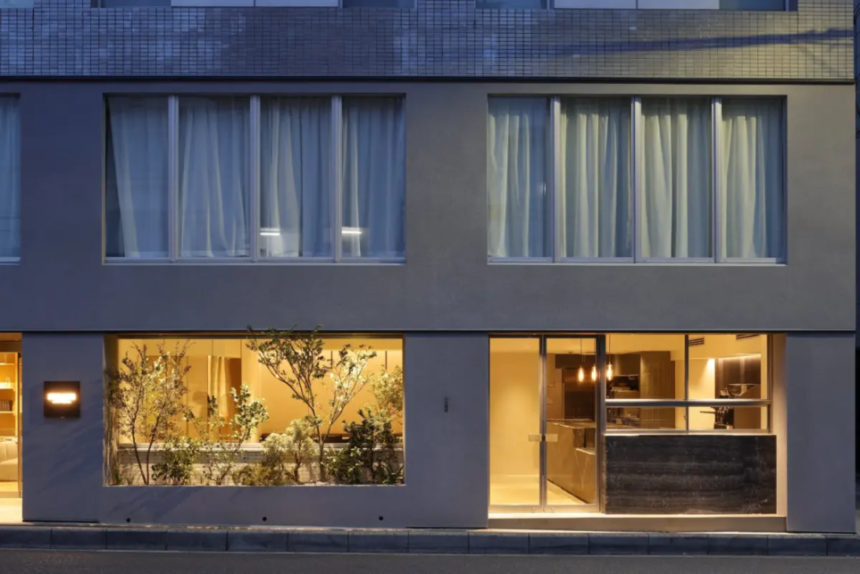 Modern twostory building facade ground floor glass windows reveal a warmly lit interior with plants and a reception area