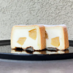Two peach filled cheesecake slices on a glossy black plate showing the creamy interior with fruit chunks inside the crust