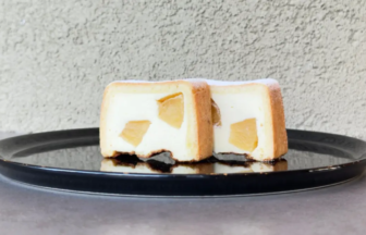 Two peach-filled cheesecake slices on a glossy black plate, showing the creamy interior with fruit chunks inside the crust.