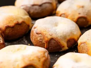 Close up of round golden brown pastries dusted with flour resting on a baking sheet