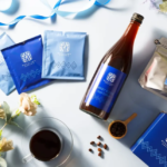 Blue packaged coffee gift set arranged on a light surface featuring coffee sachets a bottle a sealed bag a blue box beans and a cup of coffee
