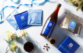 Blue-packaged coffee gift set arranged on a light surface, featuring coffee sachets, a bottle, a sealed bag, a blue box, beans, and a cup of coffee.