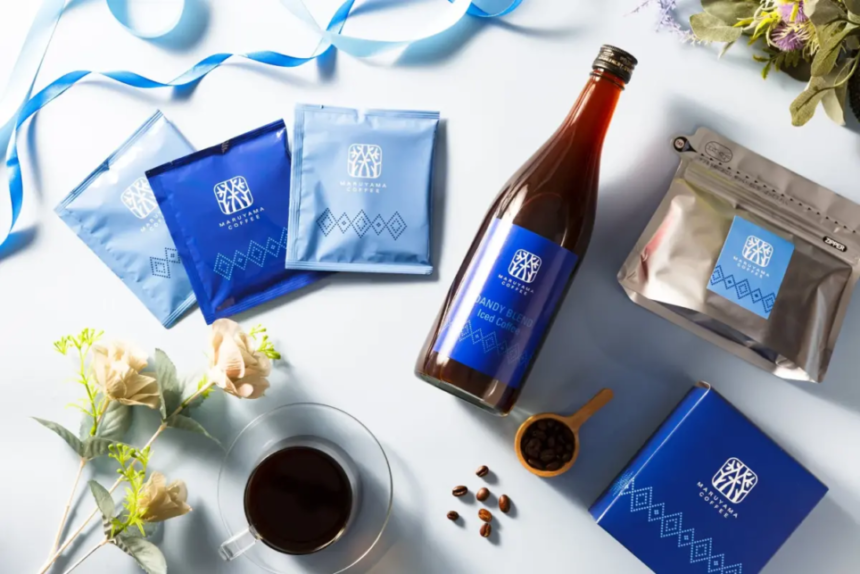 Blue packaged coffee gift set arranged on a light surface featuring coffee sachets a bottle a sealed bag a blue box beans and a cup of coffee