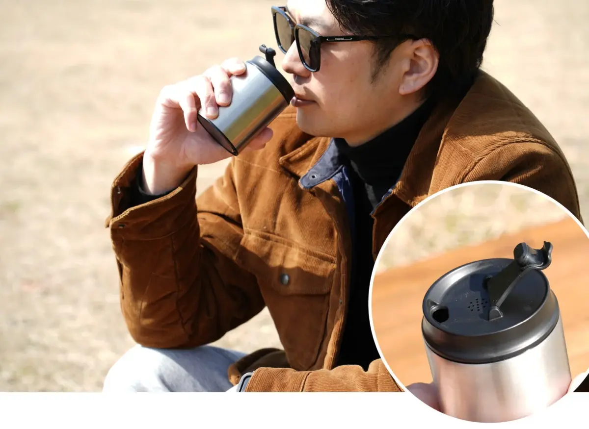 サングラスとコーデュロイジャケットを着用した男性が、屋外でステンレス製タンブラーから飲み物を飲んでいます。タンブラーの蓋のクローズアップも示されています。