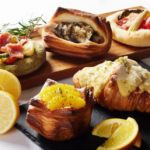 Assorted pastries on a wooden board with lemon slices and citrus topped croissants featuring savory and sweet fillings
