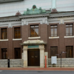 Two story brick historic building with a stone entryway and double wooden doors on a city street