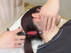Practitioner uses an Activator tool on a patients neck while stabilizing the head during a chiropractic adjustment informational