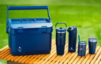 Blue cooler with a set of dark blue insulated tumblers on a wooden picnic table outdoors.