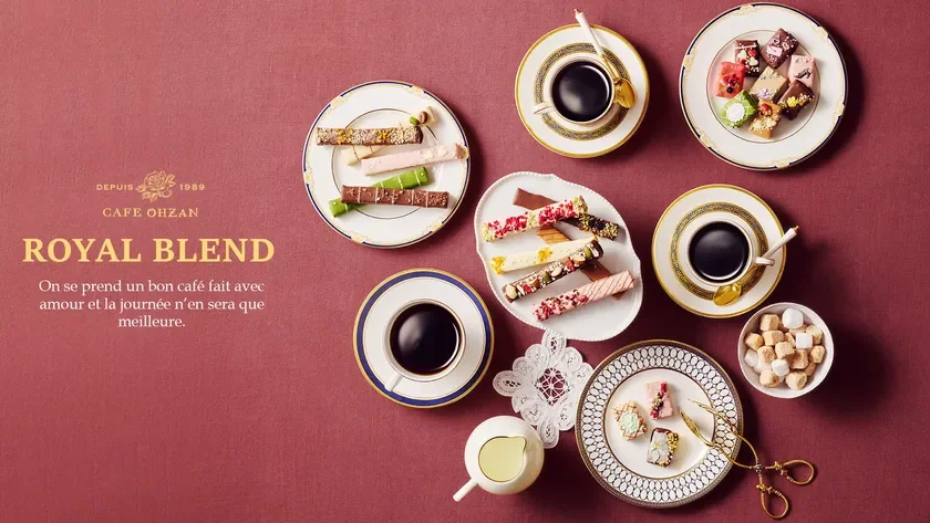 Overhead view of assorted pastries and cups of black coffee arranged on a burgundy table with ROYAL BLEND branding on the left French tagline shown