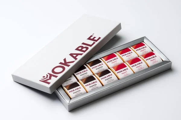 白い箱に入ったMOKABLEのチョコレートセットです。ローストとフルーティーの2種類のフレーバーが、銀色のトレイに美しく並べられています。