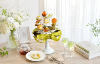 Elegant table setting with a white tiered pastry stand green ribbon floral vase and fluted glasses of green tea beside books and a plate with a bite sized treat