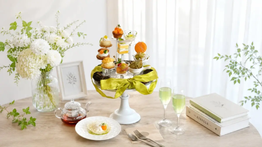 Elegant table setting with a white tiered pastry stand green ribbon floral vase and fluted glasses of green tea beside books and a plate with a bite sized treat