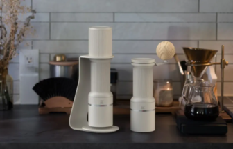 Two white coffee grinders on a dark kitchen counter a wooden ball sits on the taller unit with a pour over setup and kettle in the background