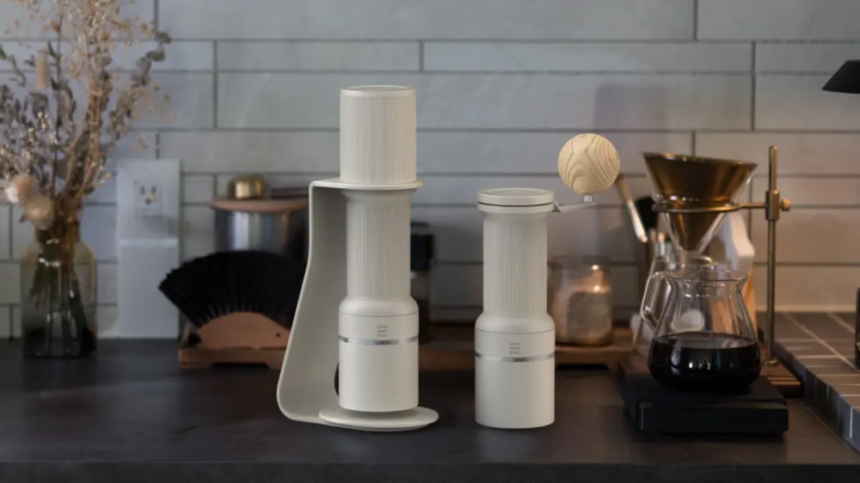 Two white coffee grinders on a dark kitchen counter a wooden ball sits on the taller unit with a pour over setup and kettle in the background