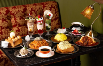 Assortment of desserts and savory dishes on a dark marble table in a cozy cafe with tall dessert parfaits cakes pasta curry rice and a cup of coffee under a desk lamp