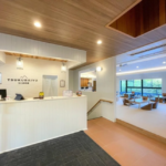 Reception desk in a bright airy lobby with a wood ceiling and a seating area visible beyond the counter