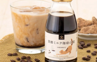 Bottle of black sugar milk coffee syrup beside a glass of iced coffee and scattered coffee beans on a burlap mat