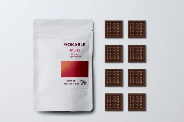 MOKABLEの「食べられるコーヒー」と書かれた白いパッケージが写っています。隣には、コーヒー豆の模様がエンボス加工された四角いチョコレートが8個きれいに並べられています。