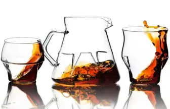 Pitcher and two whiskey glasses with amber liquid reflected on a white surface