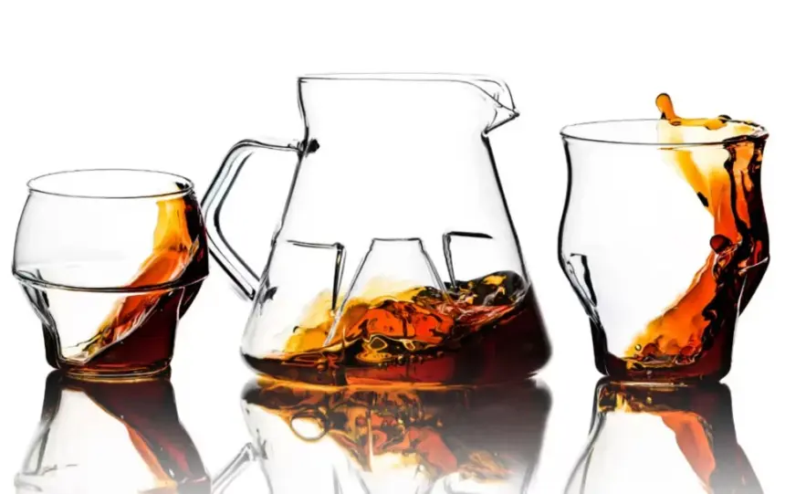 Pitcher and two whiskey glasses with amber liquid reflected on a white surface