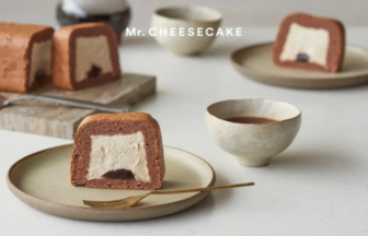 Chocolate cheesecake roll slice with white cream filling on a beige plate, brand 'Mr. Cheesecake' visible in the background.