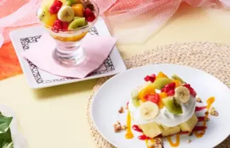 Fruit-topped dessert parfait in a glass and a mini cake with whipped cream on a plate, garnished with banana, kiwi and berries.