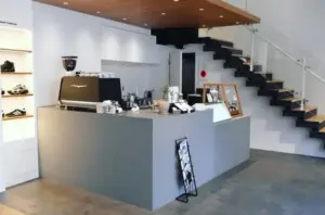 Modern cafe counter in a minimalist showroom with a coffee machine cups and a staircase to the upper level