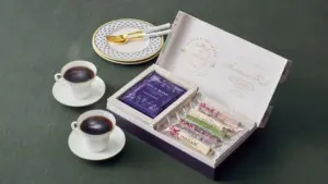 Gift tea set open box with assorted tea sachets and a cup of tea on a dark table