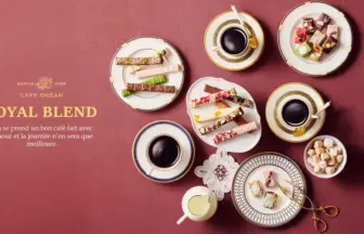Top-down view of an elegant coffee and pastry spread on a maroon table, with assorted treats and the 'ROYAL BLEND' branding on the left.