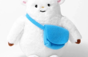White plush monster with yellow horns, brown feet, and a blue crossbody bag, facing forward with a friendly smile.