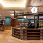 Circular coffee bar with a brick and wood counter surrounded by a ring sign that reads COFFEE BEANS with a Seagaia logo bookshelves and displays in the background
