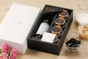 Boxed gift set with a white outer box and a black inner tray holding a bottle and five coffee jelly jars plus beverages nearby and pink flowers nearby