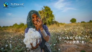 Smiling woman in a cotton field presents a fluffy cotton boll toward the camera Fair Trade logo in the top left corner