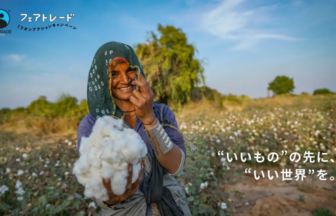 Smiling woman in a cotton field presents a fluffy cotton boll toward the camera Fair Trade logo in the top left corner