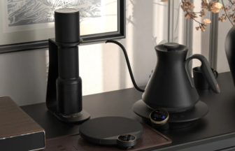 Black electric kettle on a round base on a dark kitchen counter with a vertical coffee grinder to the left