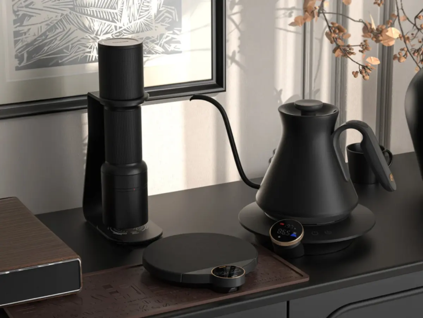 Black electric kettle on a round base on a dark kitchen counter with a vertical coffee grinder to the left